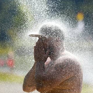 Man sieht einen Mann im Schwimmbad, der mit seiner Baseballkappe duscht.