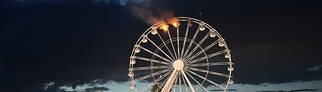 Man sieht Besucher des Highfield-Festivals, die auf ein Riesenrad blicken, an dem Flammen zu sehen sind. Auf dem Highfield-Festival am Störmthaler See ist ein Feuer an einem Riesenrad ausgebrochen.