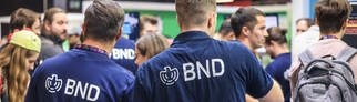 Mitarbeiter in blauen BND-T-Shirts sprechen am Stand des BND (Bundesnachrichtendienst) mit Messebesuchern.