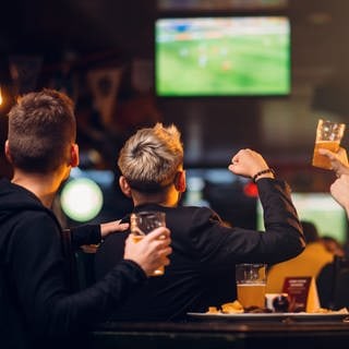 Drei Männer schauen in einer Bar Fußball. Die nächste Bundesliga-Saison beginnt jetzt mit einigen Neuerungen.