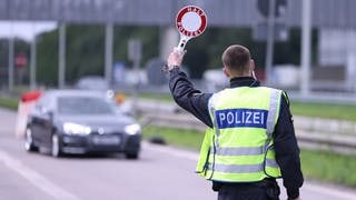 Ein Polizist hebt ein Stoppschild hoch, um an der Grenze ein Auto zu kontrollieren.