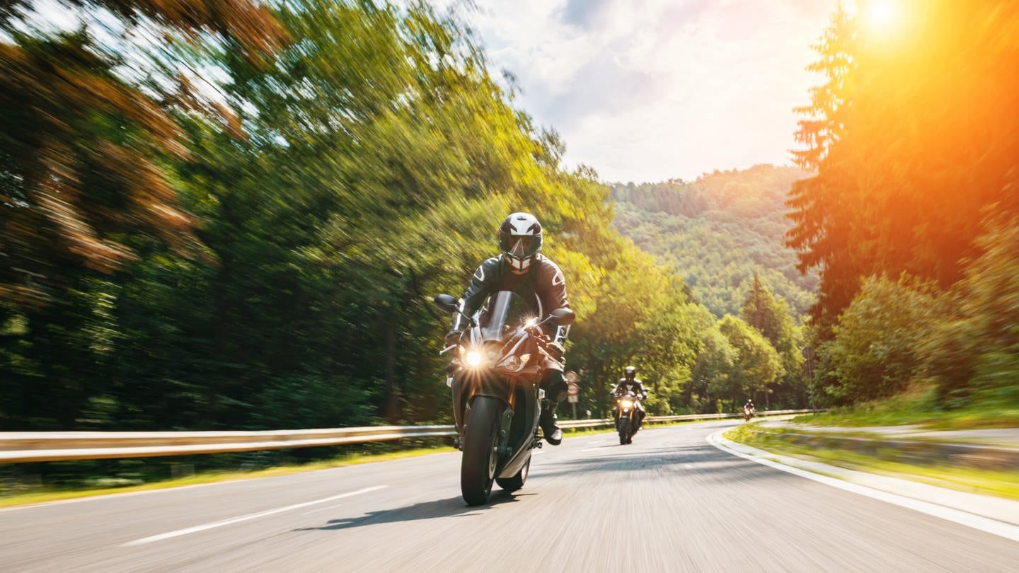 Ein Motorradfahrer fährt auf einer Straße. Im Hintergrund geht die Sonne unter.