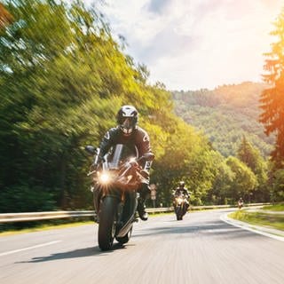 Ein Motorradfahrer fährt auf einer Straße. Im Hintergrund geht die Sonne unter.