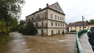 Hochwasser in Luze, Tschechien: Man sieht einen braunen Fluss, der ein altes Gebäude umfließt.