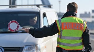 Ein Polizist hält eine Kelle und stoppt bei einer Grenzkontrolle ein Auto.