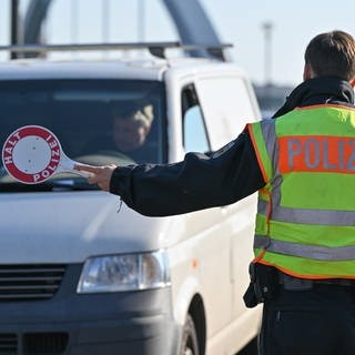 Ein Polizist hält eine Kelle und stoppt bei einer Grenzkontrolle ein Auto.