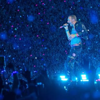 Chris Martin, Sänger der britischen Band Coldplay steht bei einem Konzert im Rahmen der „Music of the Spheres Tour 2024“ bei strömendem Regen auf der Bühne. 