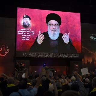 Anhänger erheben ihre Fäuste und jubeln, während sie eine Rede des Hisbollah-Führers Nasrallah auf einem Bildschirm verfolgen.