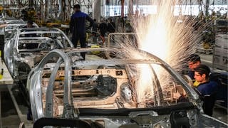 An einer Karosserie schweißen Arbeiter im Karosseriebau Mercedes-Benz-Modelle zusammen während Funken umherfliegen.