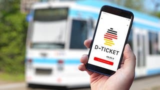 Das Deutschlandticket auf einem Handy vor einem Bus. Noch kostet es 49 Euro, ab 2025 wird das Ticket teurer.