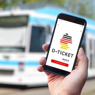 Das Deutschlandticket auf einem Handy vor einem Bus. Noch kostet es 49 Euro, ab 2025 wird das Ticket teurer.