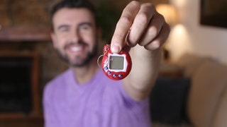 Ein Mann hält ein Tamagotchi in seiner Hand.