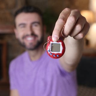 Ein Mann hält ein Tamagotchi in seiner Hand.