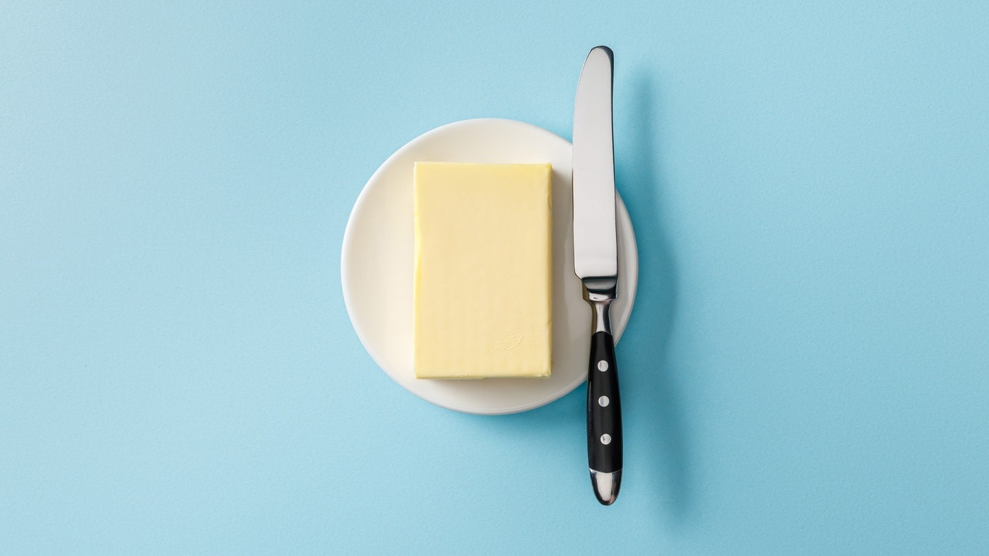 Block Butter auf einem weißen Teller vor einem hellblauen Hintergrund | Symbolbild für die steigenden Butterpreise im Supermarkt