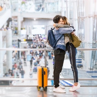 Zwei Personen umarmen sich am Flughafen. Schon 20 Sekunden sollen reichen um Oxytocin auszuschütten.