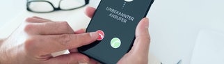 Ein Mann drückt auf einem Smartphone, auf dem ein unbekannter Anrufer anruft, auf den Auflegen-Button.