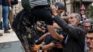 König Felipe VI. (r) von Spanien spricht bei seinem Besuch in einem von den Überschwemmungen betroffenen Gebiet mit Menschen und hält einen jungen Mann um den Nacken und an der Hand.