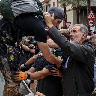 König Felipe VI. (r) von Spanien spricht bei seinem Besuch in einem von den Überschwemmungen betroffenen Gebiet mit Menschen und hält einen jungen Mann um den Nacken und an der Hand.