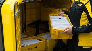 Eine Mitarbeiterin der Post hebt eine Kiste Briefe ins Postauto. (Symbolbild)