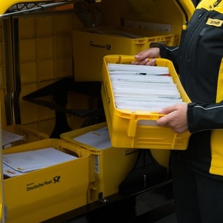 Eine Mitarbeiterin der Post hebt eine Kiste Briefe ins Postauto. (Symbolbild)