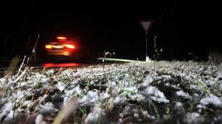 Ein Auto fährt am Abend neben einer schneebedeckten Wiese.