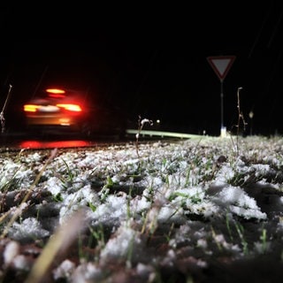 Ein Auto fährt am Abend neben einer schneebedeckten Wiese.