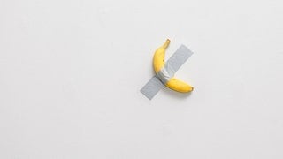 Eine Banane klebt mit Klebeband an der Wand, ein Kunstwerk von Maurizio Cattelan.