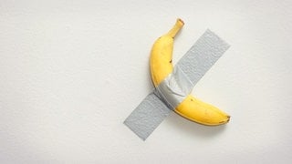 Eine Banane klebt mit Klebeband an der Wand, ein Kunstwerk von Maurizio Cattelan.