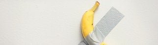 Eine Banane klebt mit Klebeband an der Wand, ein Kunstwerk von Maurizio Cattelan.