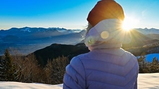 Eine Frau steht bei Sonnenaufgang auf dem Mitterberg in Oberbayern. Hier liegt Anfang Dezember schon Schnee.