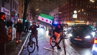 Zwei Syrer auf Fahrrädern und mit syrischer Flagge feiern den Sturz Assads in Berlin-Neukölln.