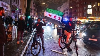 Zwei Syrer auf Fahrrädern und mit syrischer Flagge feiern den Sturz Assads in Berlin-Neukölln.