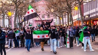 Syrer feiern in Deutschland mit schwenkenden Fahnen den Sturz von Assad.