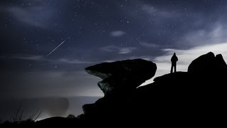 Ein Mann beobachtet einen Meteor über der Felsformation Brimham Rocks in England während des Geminiden-Meteoritenschauers.