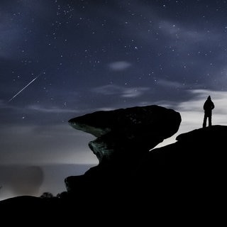 Ein Mann beobachtet einen Meteor über der Felsformation Brimham Rocks in England während des Geminiden-Meteoritenschauers.