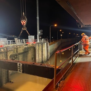 Arbeiter stehen an der provisorischen Mosel-Schleuse, ein Taucher schwimmt im Wasser