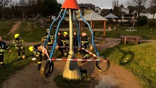 Feuerwehrleute sperren ein Spielgerät auf einem Spielplatz in Hackenheim mit Flatterband ab