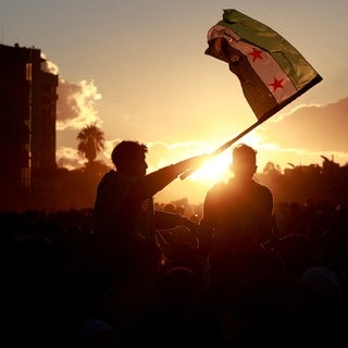 Mann schwenkt eine syrische Flagge: Nach dem Sturz von Assad gab es die erste Demonstration in Damaskus für Demokratie und Freiheit