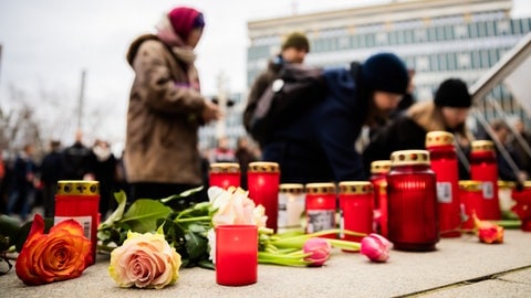 Menschen legen bei einer Mahnwache auf dem Platz vor der Oper Blumen und Kerzen nieder.