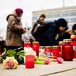 Menschen legen bei einer Mahnwache auf dem Platz vor der Oper Blumen und Kerzen nieder.