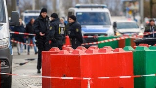 Absperrband vor farbigen Betonsperren auf dem Weihnachtsmarkt in Magdeburg. Dahinter Polizisten, die nach dem mutmaßlichen Anschlag ermitteln.