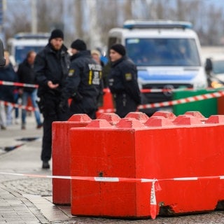 Absperrband vor farbigen Betonsperren auf dem Weihnachtsmarkt in Magdeburg. Dahinter Polizisten, die nach dem mutmaßlichen Anschlag ermitteln.