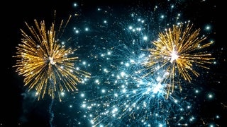 Gelbes und weißes Feuerwerk am dunklen Nachthimmel. An Silvester gilt wieder teilweise Böllerverbot.