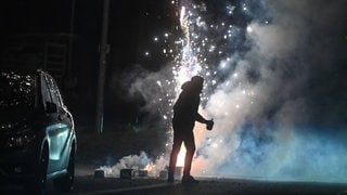 Ein Mann steht an Silvester vor Feuerwerk mit einem Böller in der Hand