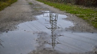 Ein Strommast spiegelt sich in einer Wasserpfütze auf einem Weg