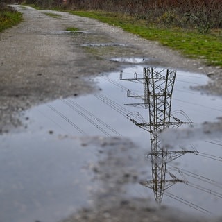 Ein Strommast spiegelt sich in einer Wasserpfütze auf einem Weg