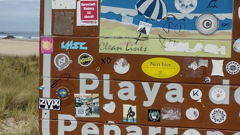 Ein „Nett hier“-Aufkleber klebt an einem Schild am Strand Playa de Peñaronda in Santa Gadea, Tapia de Casariego, Asturien, Spanien.