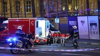 Ein Feuerwehrmann wird von Polizeibeamten unterstützt, um eine verletzte Person auf einer Trage vor dem Straßburger Bahnhof zu transportieren, nachdem zwei Straßenbahnen zusammengestoßen sind.