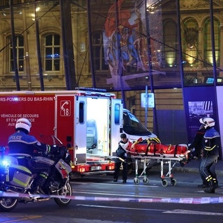 Ein Feuerwehrmann wird von Polizeibeamten unterstützt, um eine verletzte Person auf einer Trage vor dem Straßburger Bahnhof zu transportieren, nachdem zwei Straßenbahnen zusammengestoßen sind.