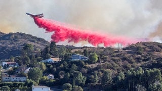 Ein Flugzeug der Feuerwehr wirft Wasser mit rotem Brandhemmer über dem Palisades Fire bei Los Angeles ab